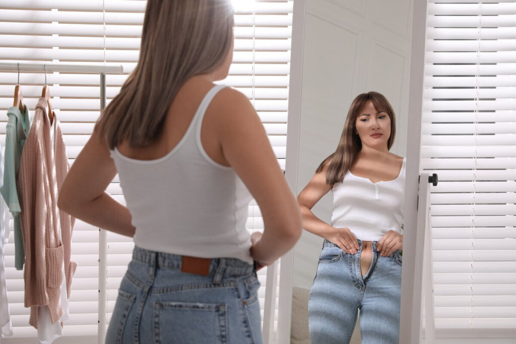 Mulher colocando calça jeans em frente a um espelho