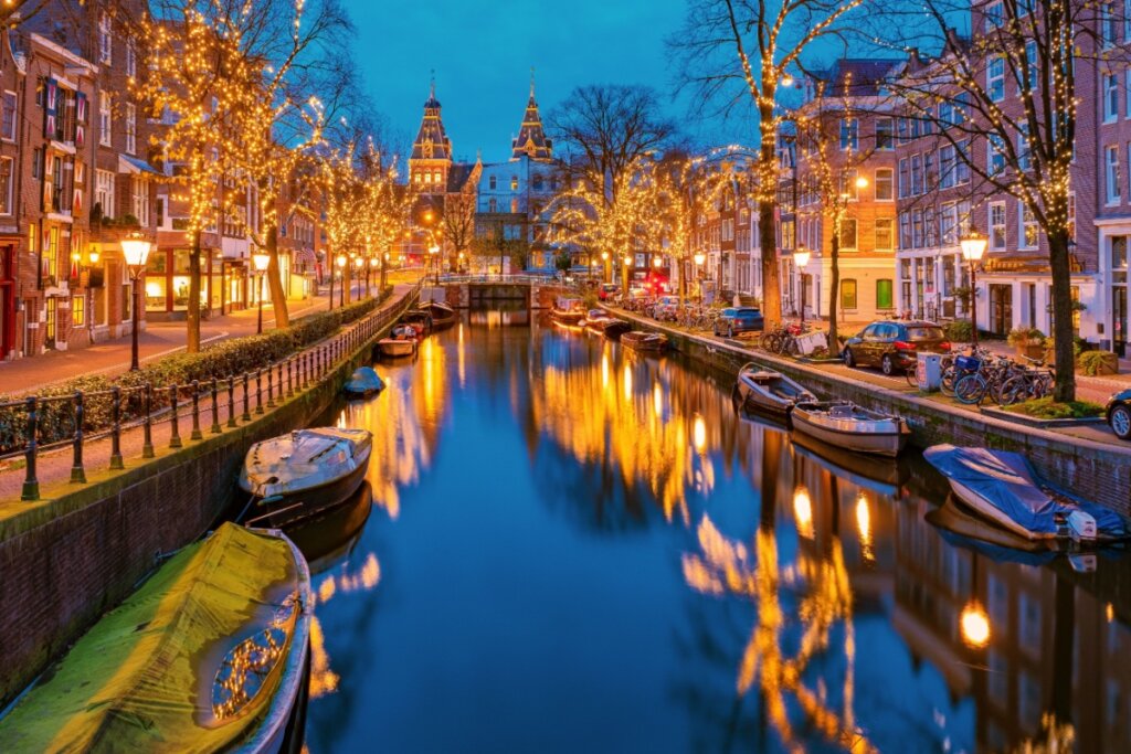 Canal em Amsterdã; ao redor, árvores iluminadas e casas