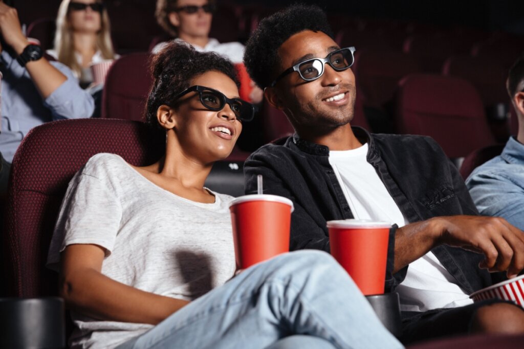 Homem e mulher no cinema com óculos 3D e copos nas mãos