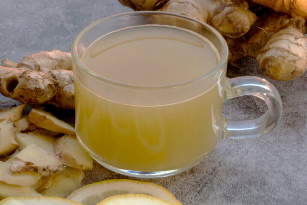 Recipiente transparente com chá e gengibre e pedaços de limão espalhados em volta