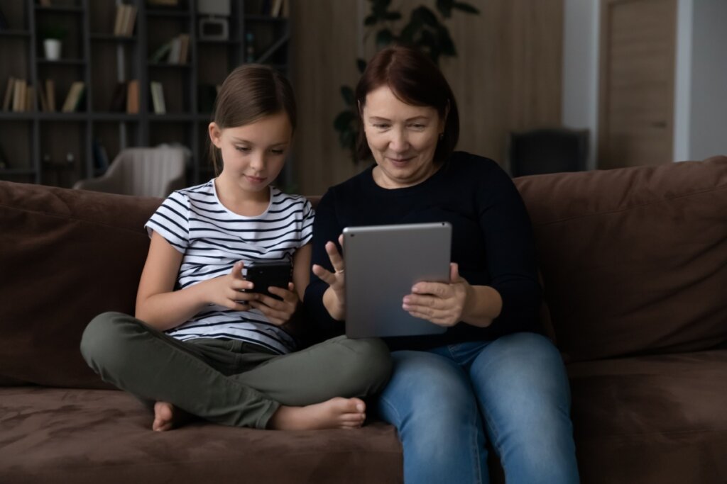 Criança e avó usando internet sentadas em um sofá