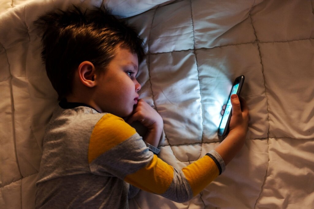 Criança usando o celular deitada na cama.