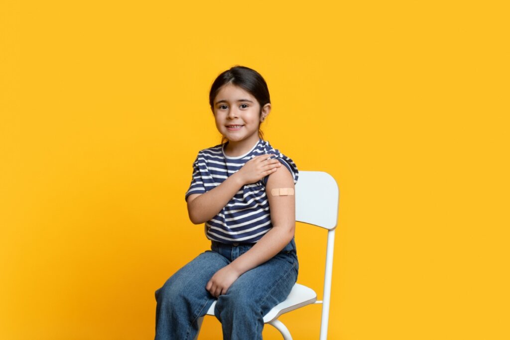 Menina sentada em cadeira mostrando braço com curativo de vacina