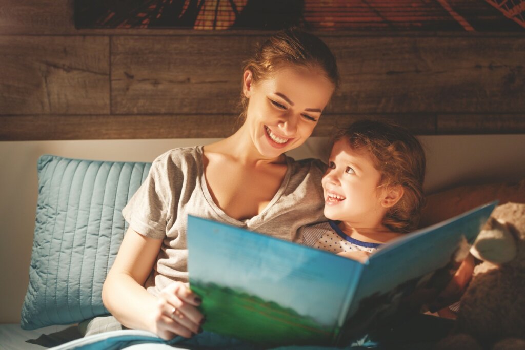 Mulher sorrindo lendo livro para criança na cama