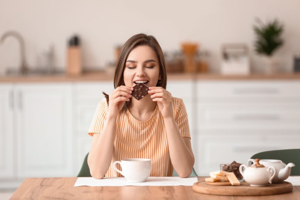 Mulher comendo chocolate em uma cozinha.
