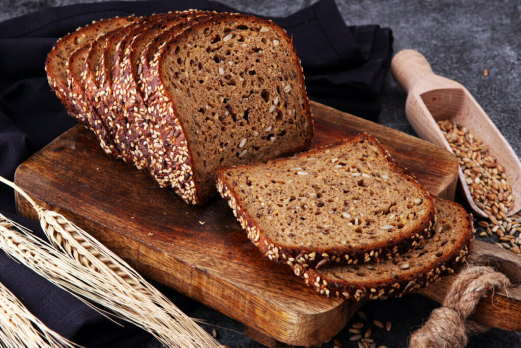 Pão integral com grãos fatiado em cima de uma tábua de madeira