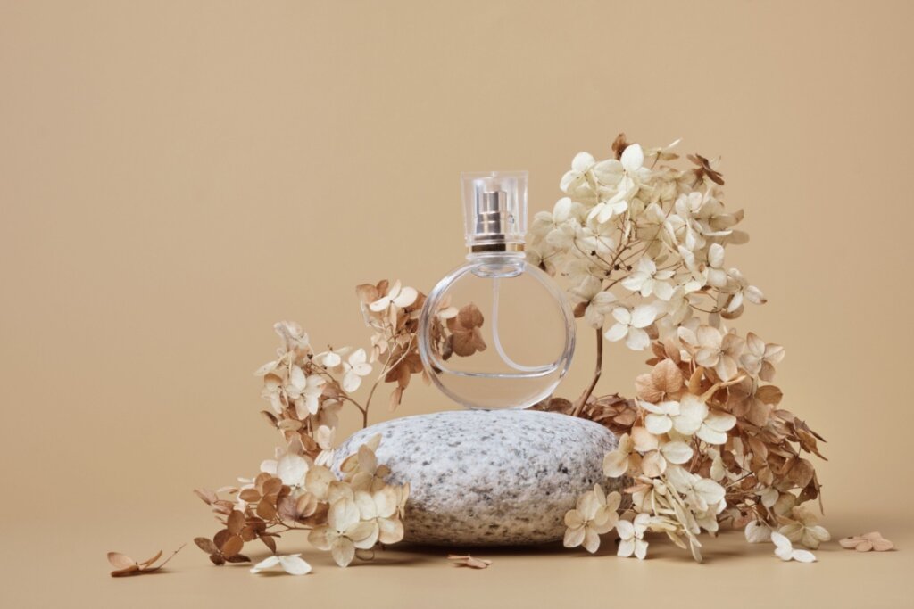 Perfume em cima de uma pedra com flores secas ao lado em um fundo bege.
