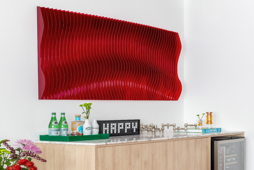 ambiente com um quadro vermelho em relevo que dá a impressão de ondas acima de um armário em madeira