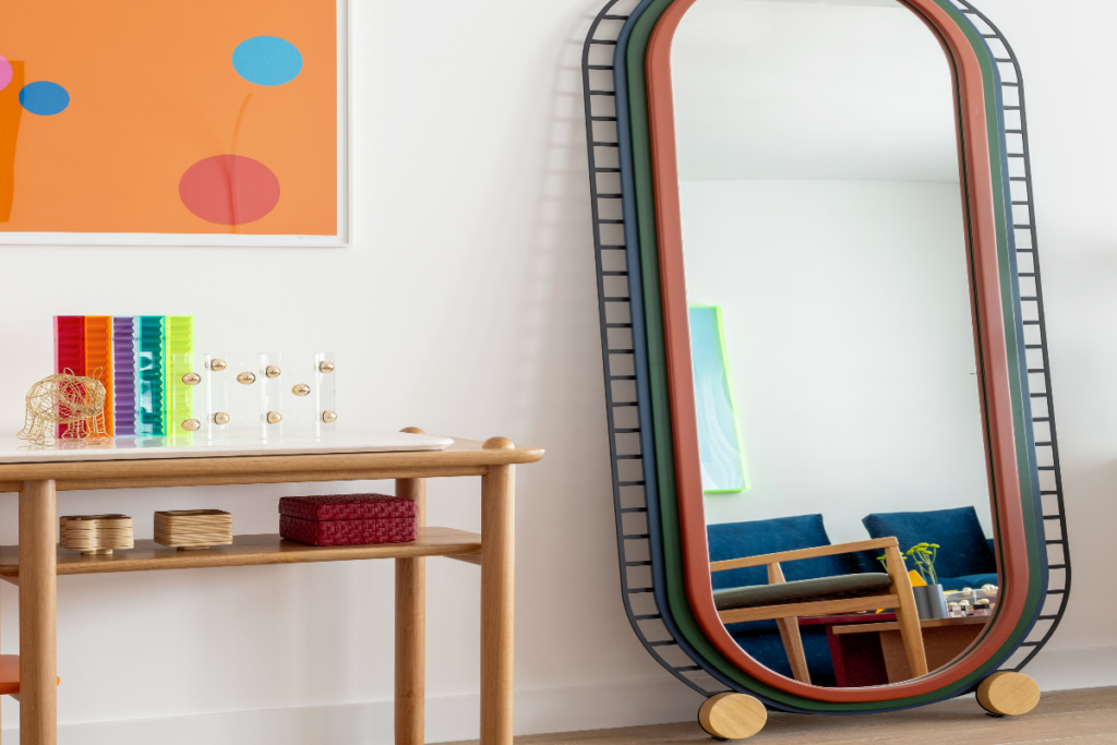 espelho com moldura colorida ao lado de móvel de madeira 