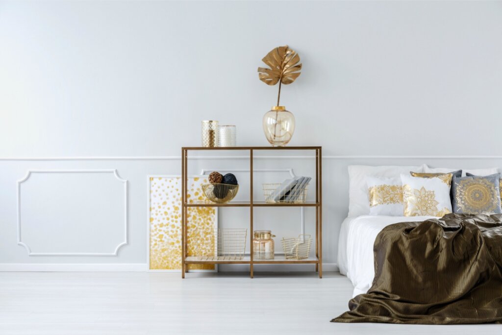 Imagem de quarto com detalhes dourados na cama e na estante ao lado dela 