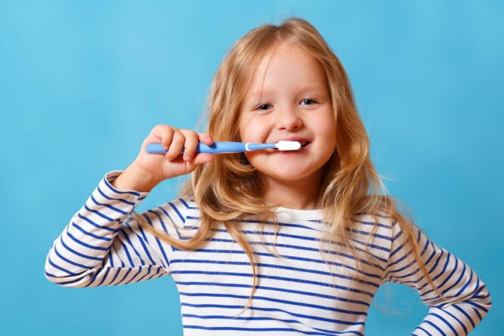 Menina com uma escova de dentes na boca em frente a um fundo azul