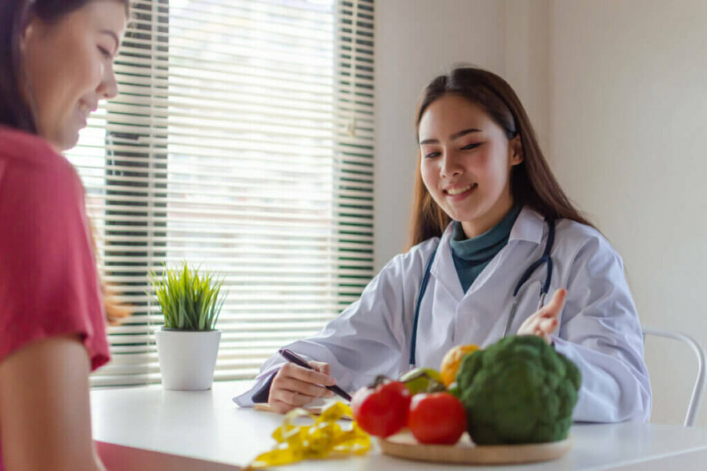 Médica sentada em frente de frutas e vegetais 