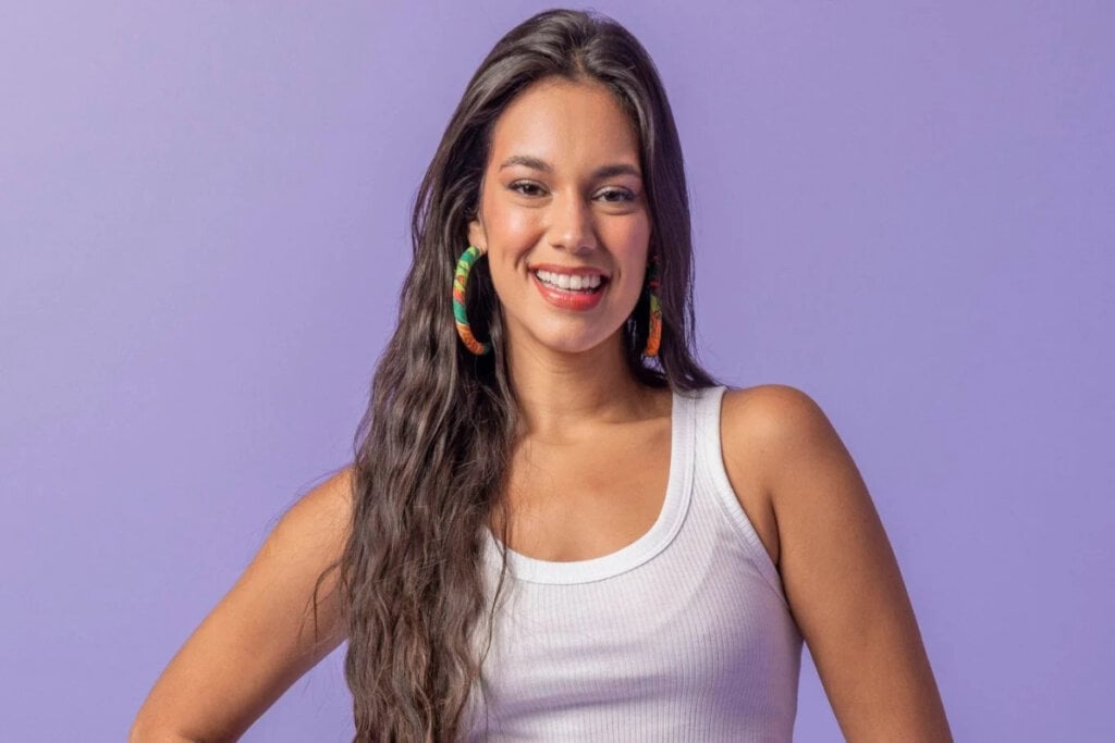 Alane de camiseta branca e sorrindo em fundo roxo