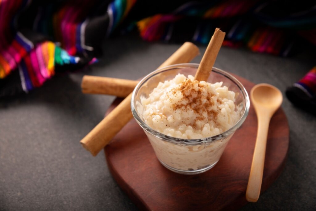 arroz-doce com canela em potinho de vidro e colher de pau ao lado 