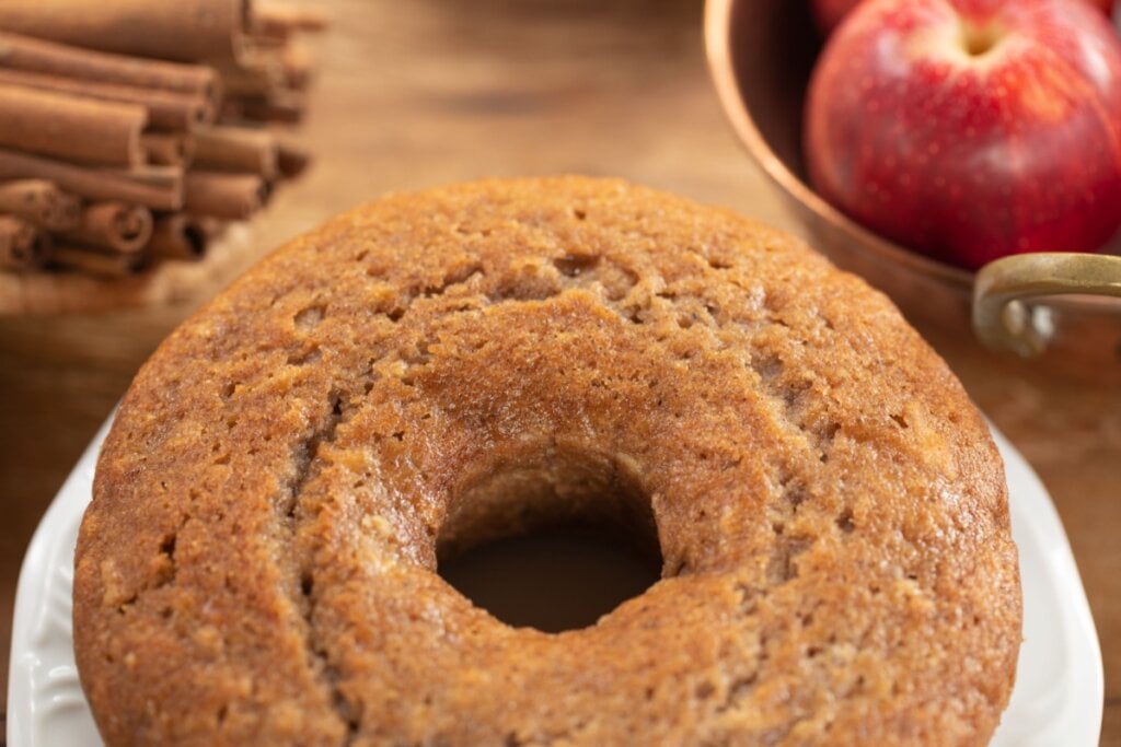 bolo de maçã e canela redondo com furo no meio e maçã e canela em pau ao fundo