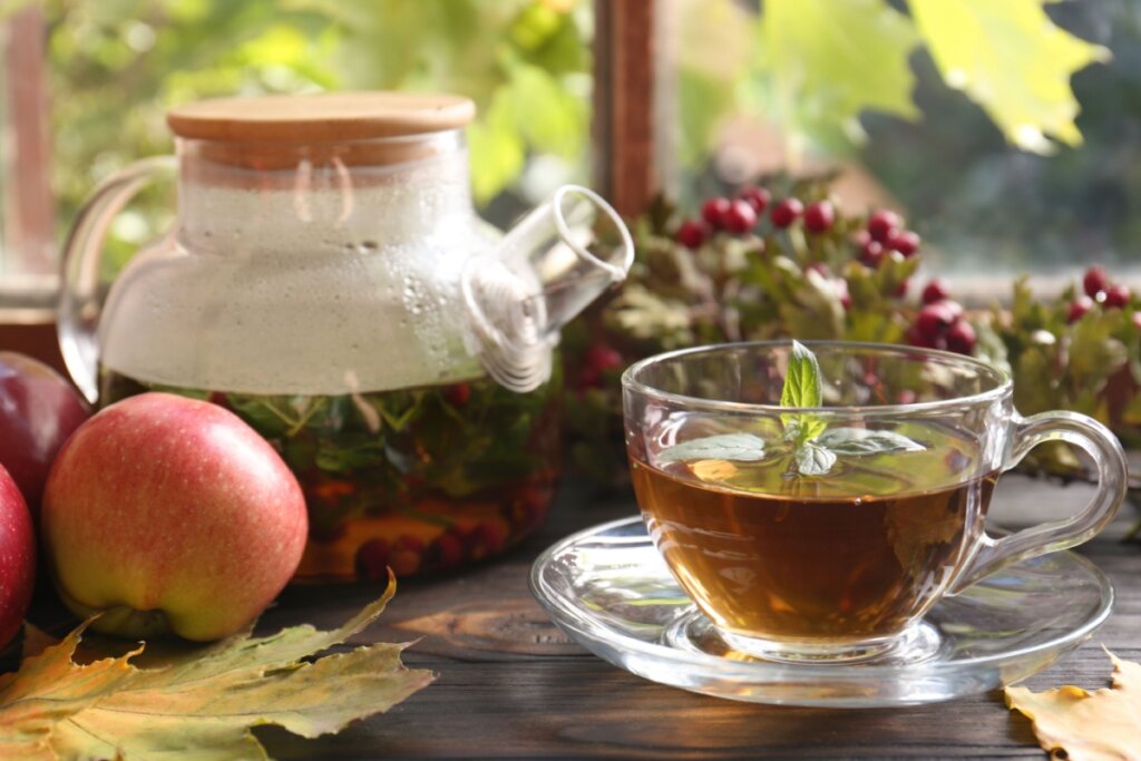 Chá de maçã em xícara de vidro com chaleira ao fundo e maçãs