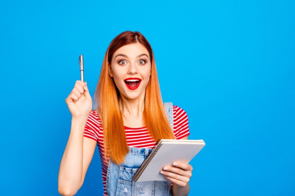 Menina com batom vermelho e boca aberta segurando lápis e caderno