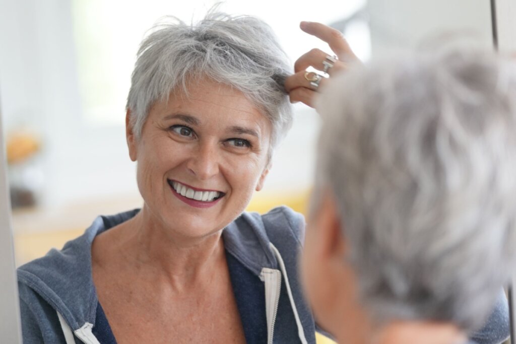 Mulher com cabelo grisalho se olhando no espelho