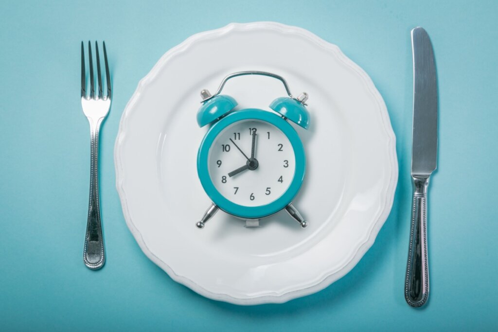 Relógio azul em cima de prato branco com garfo e faca ao lado