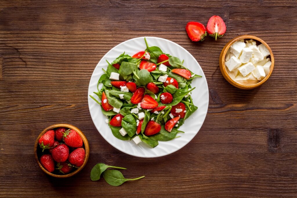 Salada de morango e espinafre em prato e morango e espinafre separados em recipientes diferentes ao lado do prato