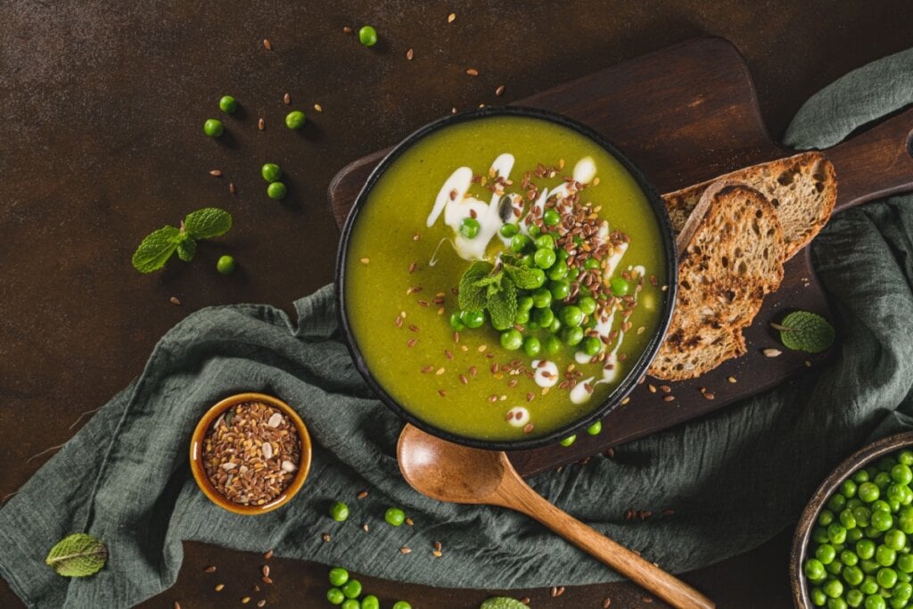 Recipiente preto com sopa verde de ervila com linha, hortelã e iogurte em cima