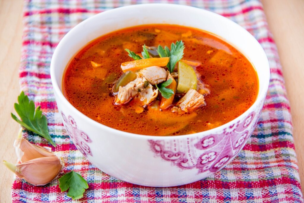 Pote branco com sopa de frango e vegetais com caldo vermelho 