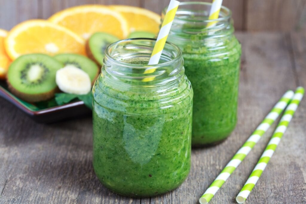 Suco verde em copo de vidro com laranja, kiwi e espinafre ao fundo