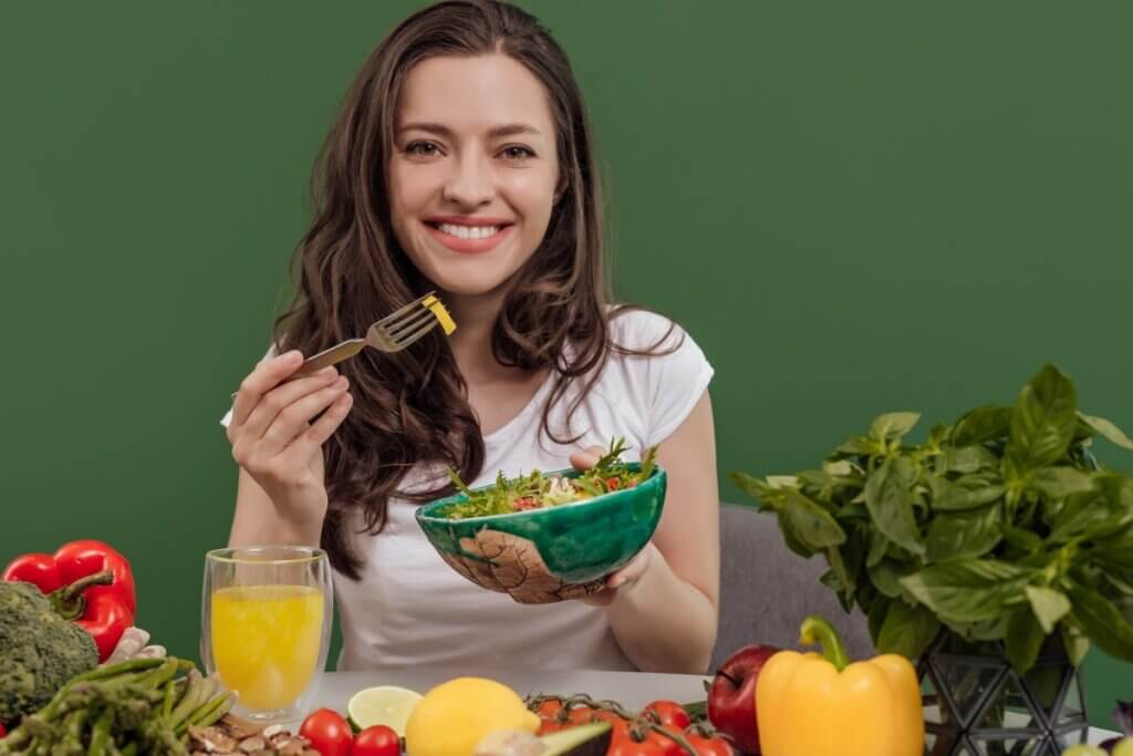 Mulher segurando um recipiente com salada em frente a uma mesa com alimentos e suco