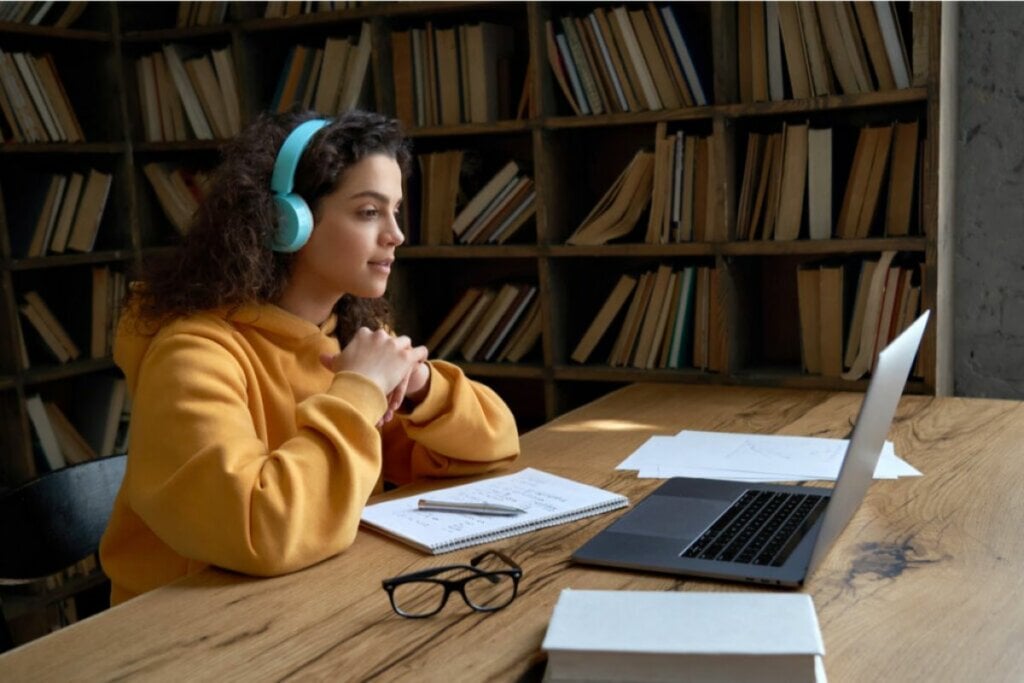 Menina estudando com o notebook aberto e cadernos abertos em cima da mesa