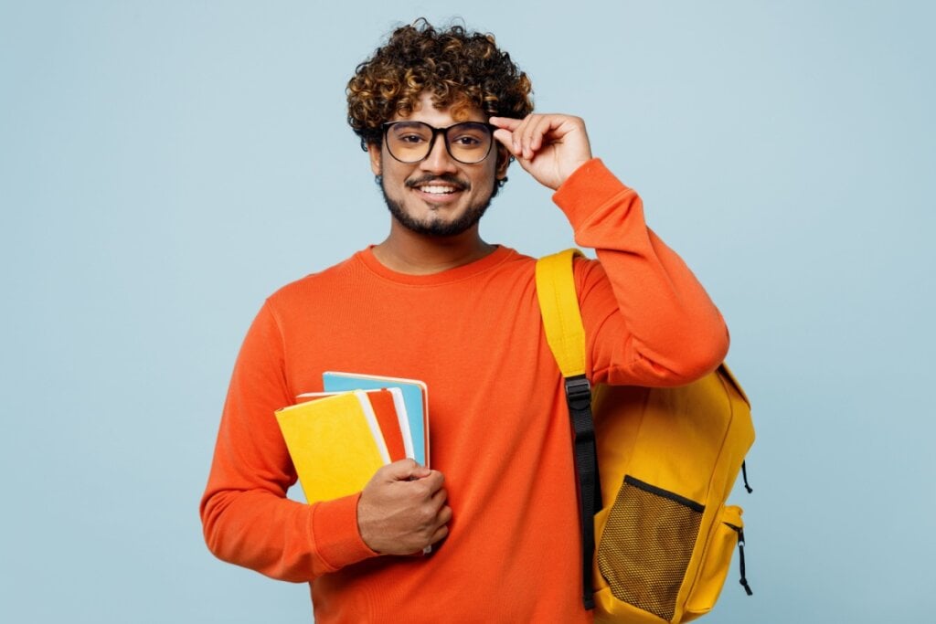 Estudante sorrindo segurando livros com mochila em outro braço