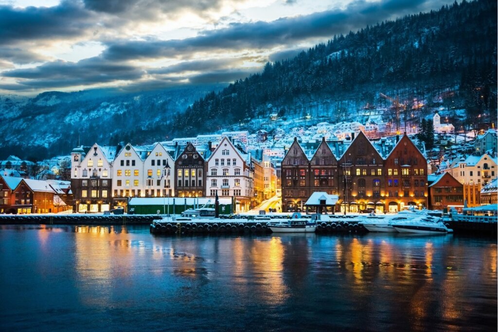 Cidade na Noruega  com mar a frente, casas ao meio e montanhas ao fundo
