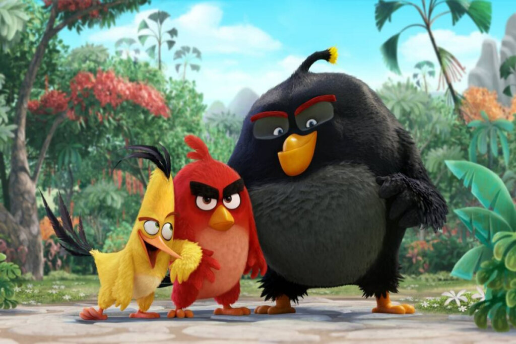 Três pássaros encaram a câmera, um é amarelo, outro, vermelho, e outro preto; ao fundo, uma floresta
