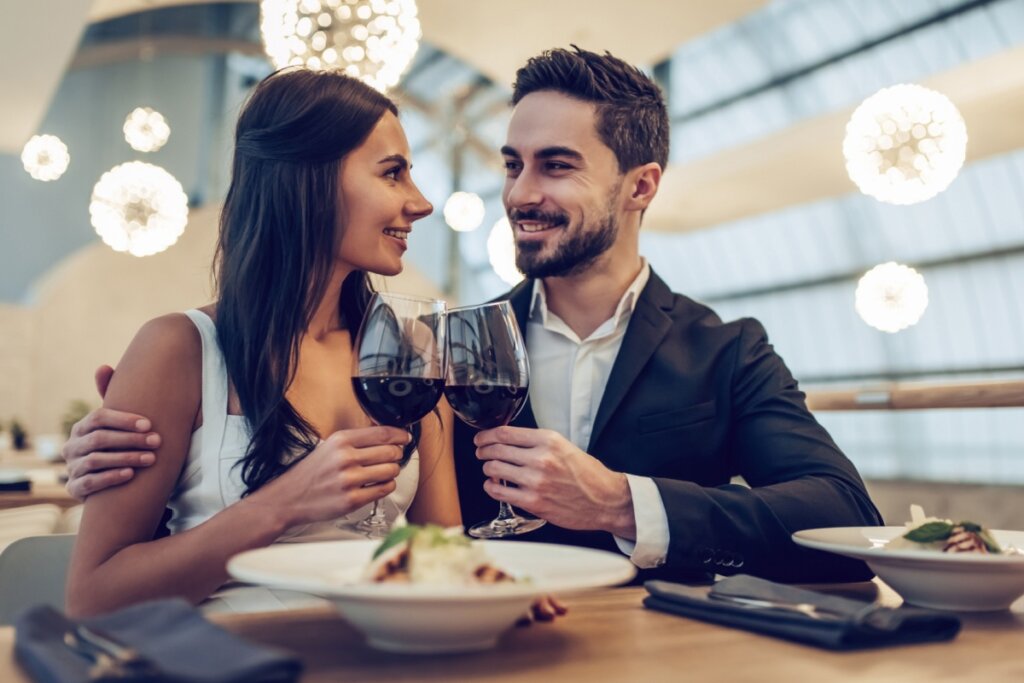 Casal em restaurante brindando com taça de vinho e se olhando