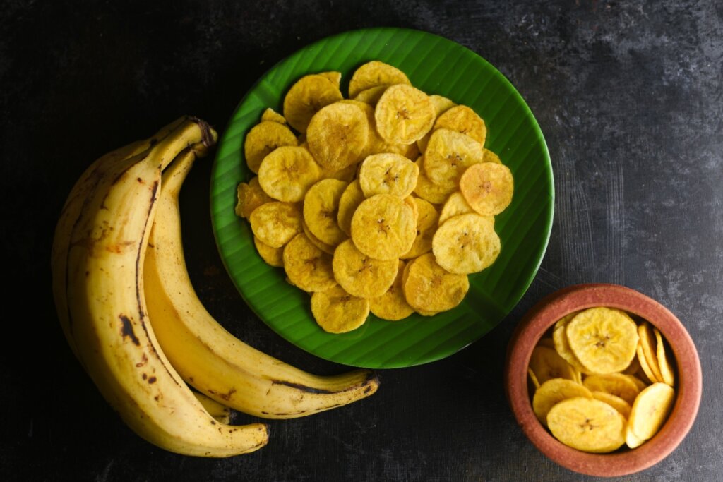 Chips de banana em dois recipientes e bananas-da-terra ao lado de um deles