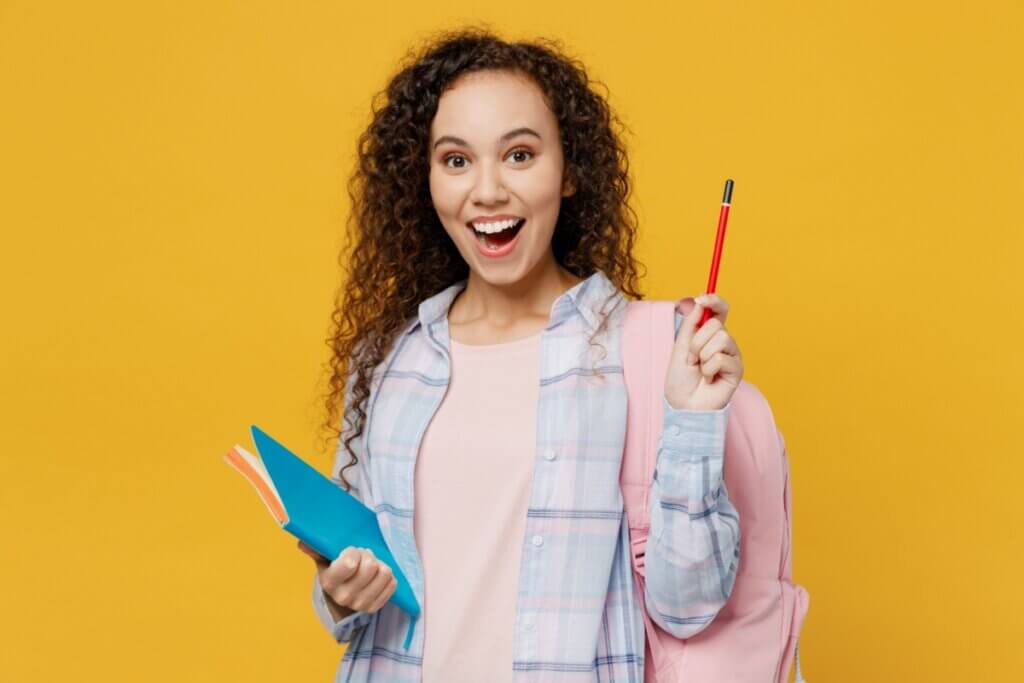 Estudante com mochila nas costas, lápis e caderno na mão em fundo amarelo