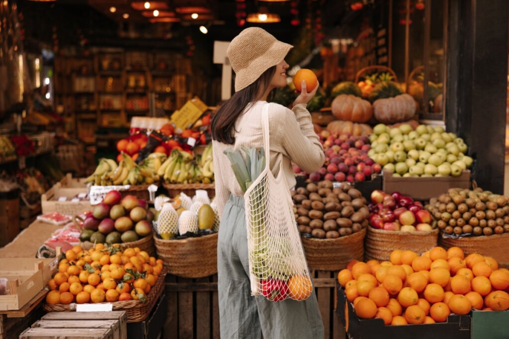 Menina em frente à banca de frutas e cheirando laranja