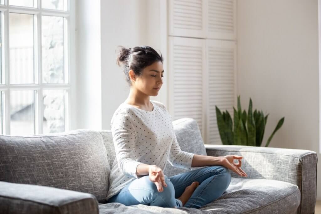 Mulher sentada em sofá meditando com os olhos fechados