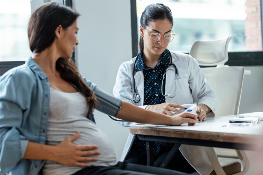 mulher grávida em consultório com uma médica aferindo a pressão.
