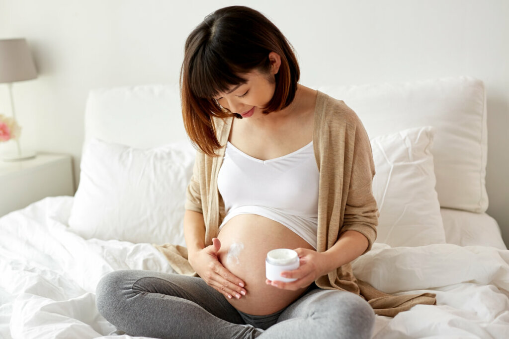 Mulher grávida com mão na barriga e segurando creme