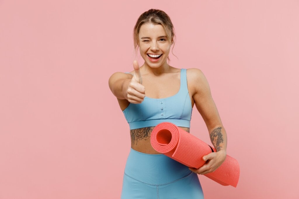 Mulher com roupa de pilates segurando tapete para fazer exercícios