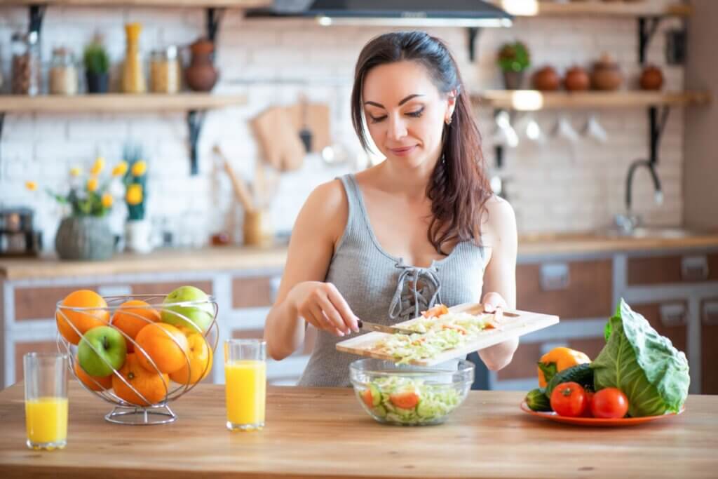 mulher em bancada com diversos alimentos fazendo uma salada