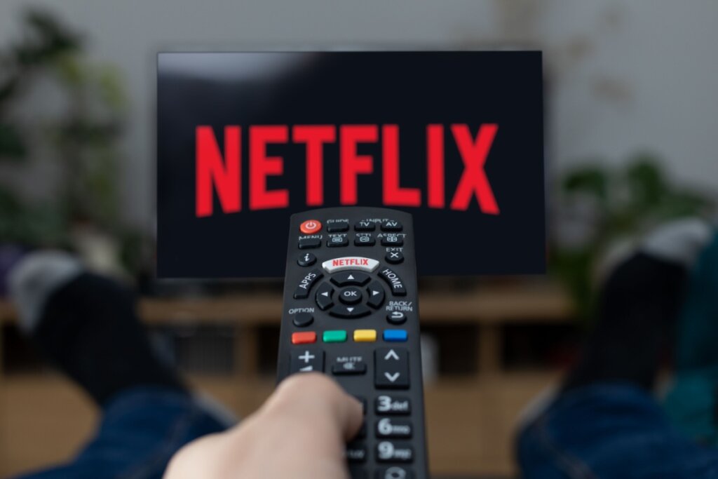 Mão com controle remoto apontando para TV com logo da Netflix