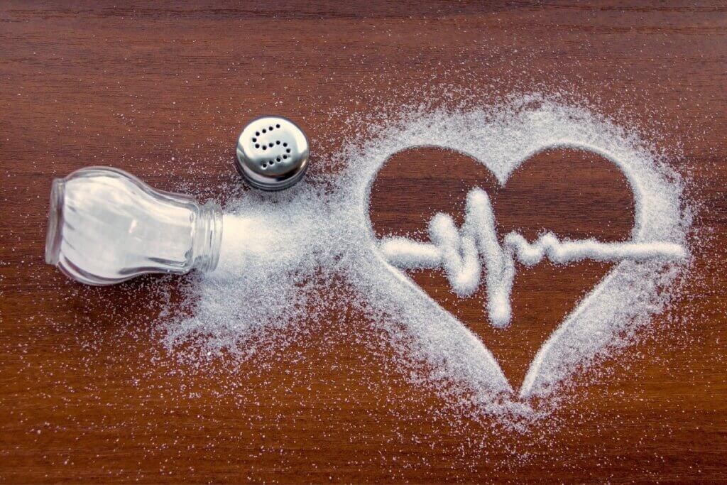 um pote de sal derramado e na bancada de madeira formando um coração e um batimento cardíaco dentro do coração