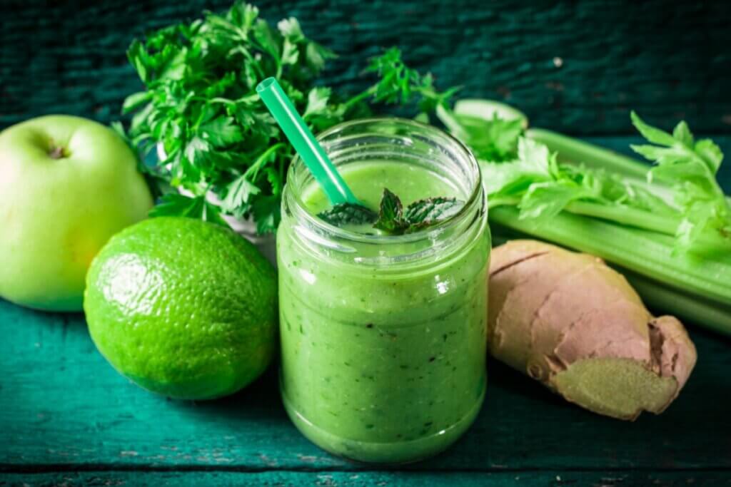 Suco verde em copo de vidro com limão, gengibre e aipo em volta