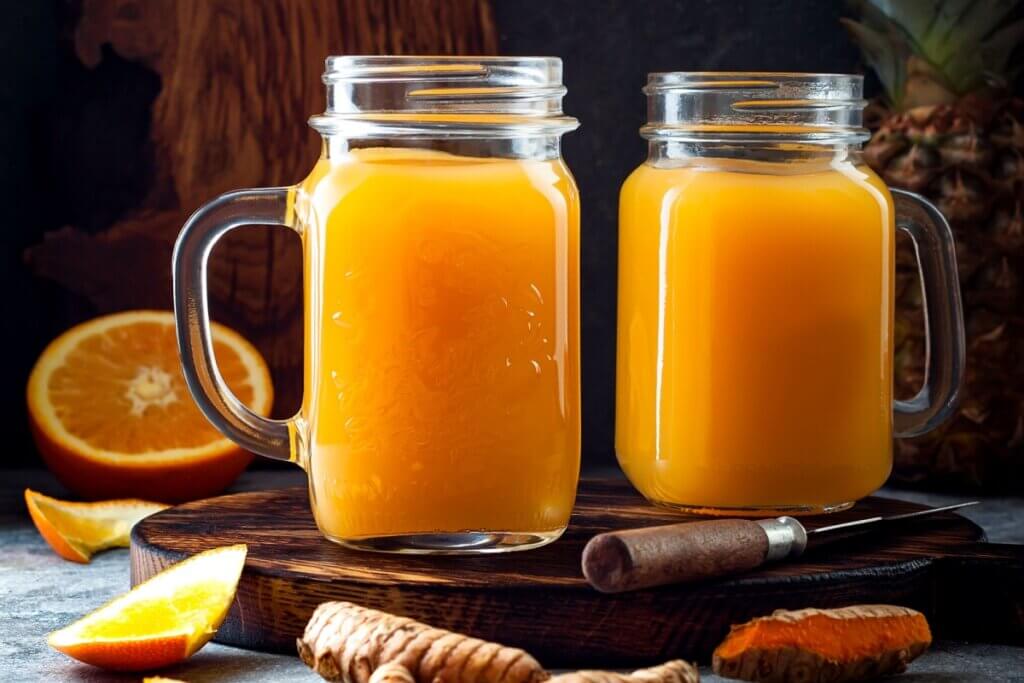 Dois copos de vidro em cima de tábua com suco laranja