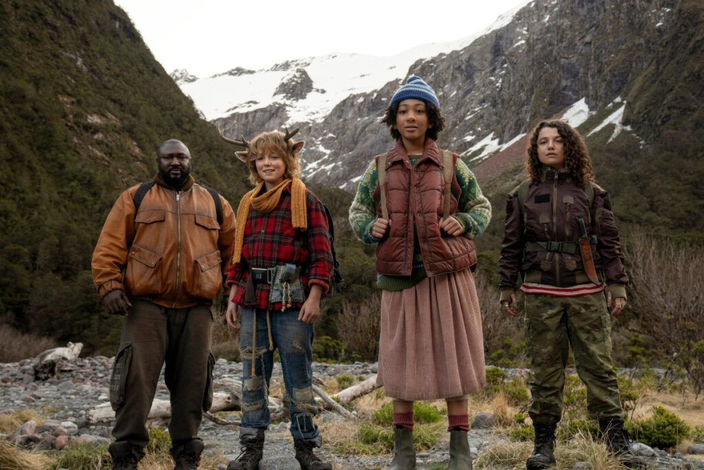 4 pessoas uma ao lado da outra com roupas de inverno em uma região montanhosa olhando para frente com expressões de preocupação e esperança