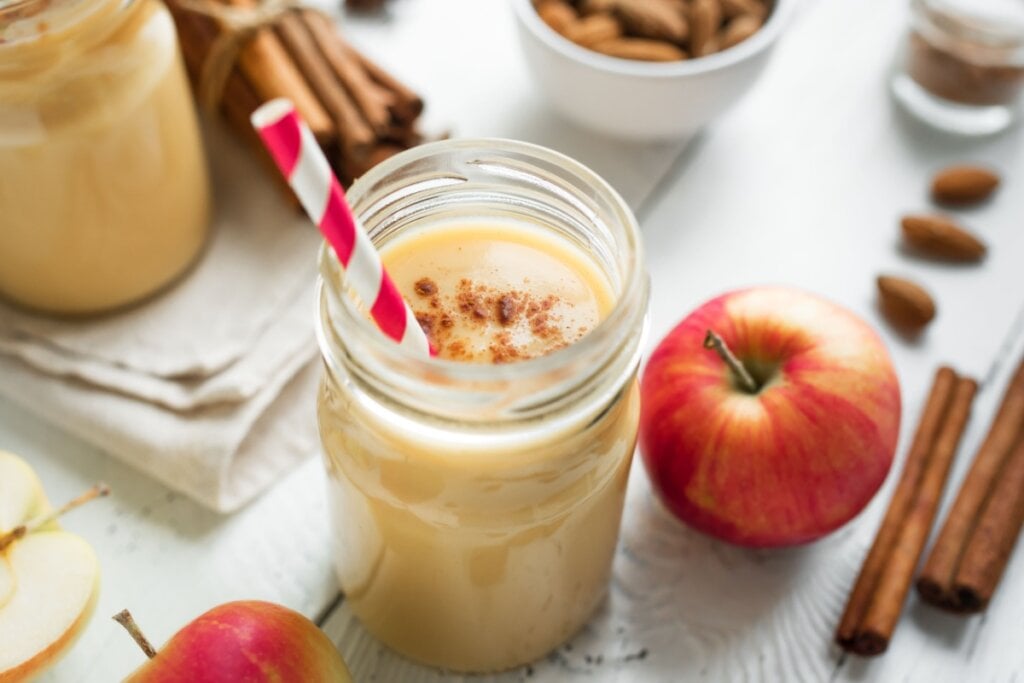 Copo de vidro com vitamina de maçã e canela com maçã e canela ao lado