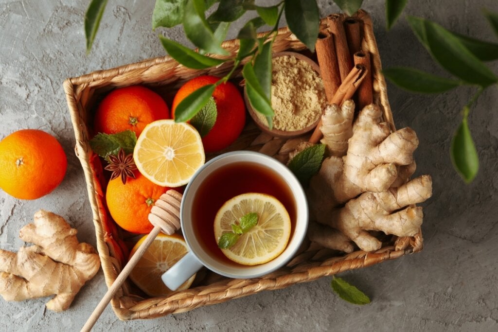 Cesta de madeira com uma xícara com chá e rodela de laranja com laranjas, canela em pau e gengibre ao redor