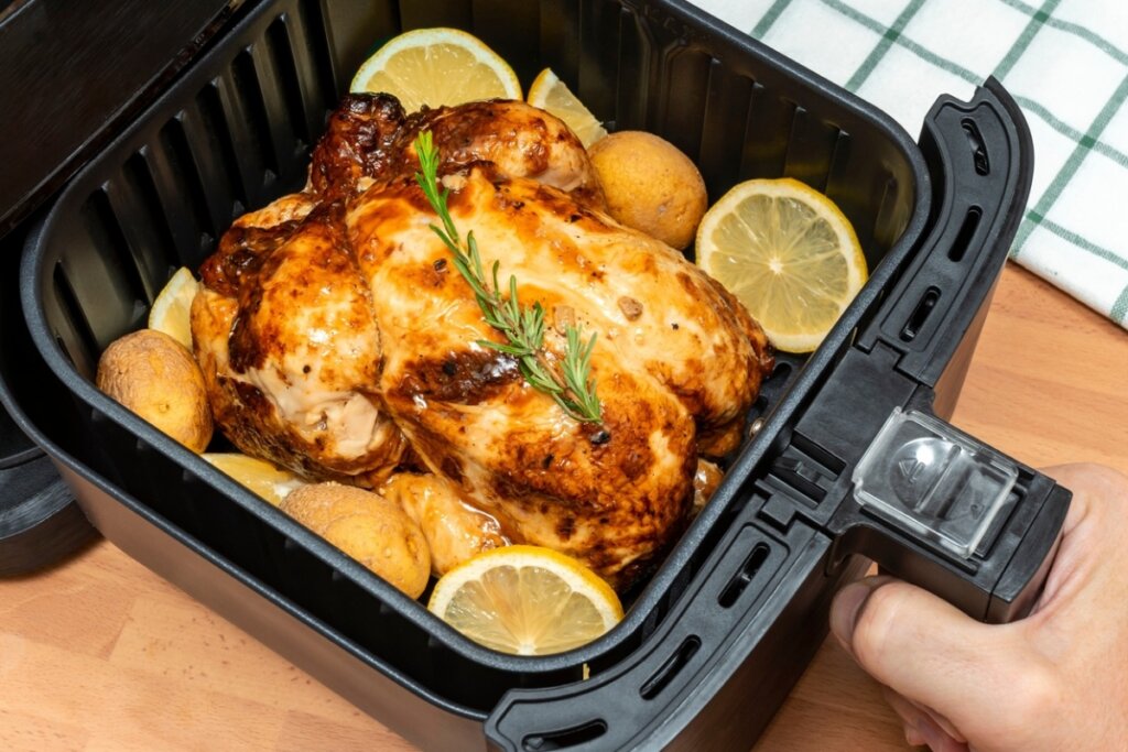 Frango inteiro na cesta de uma airfryer com batata-bolinha e rodelas de laranja