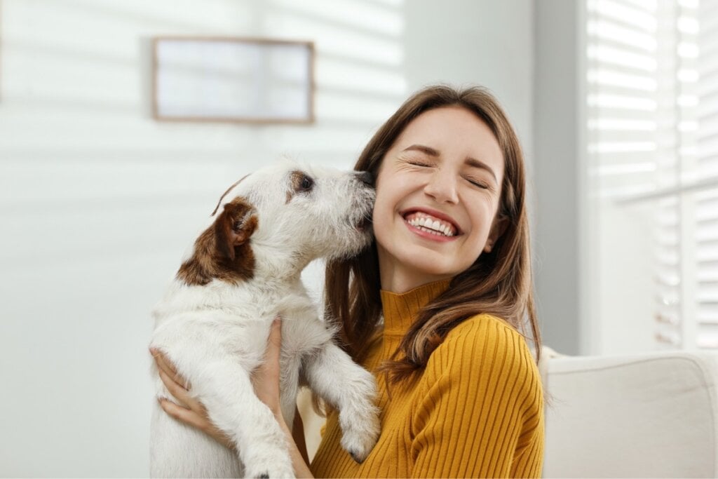 Cachorro lambendo o rosto de uma mulher enquanto ela sorri